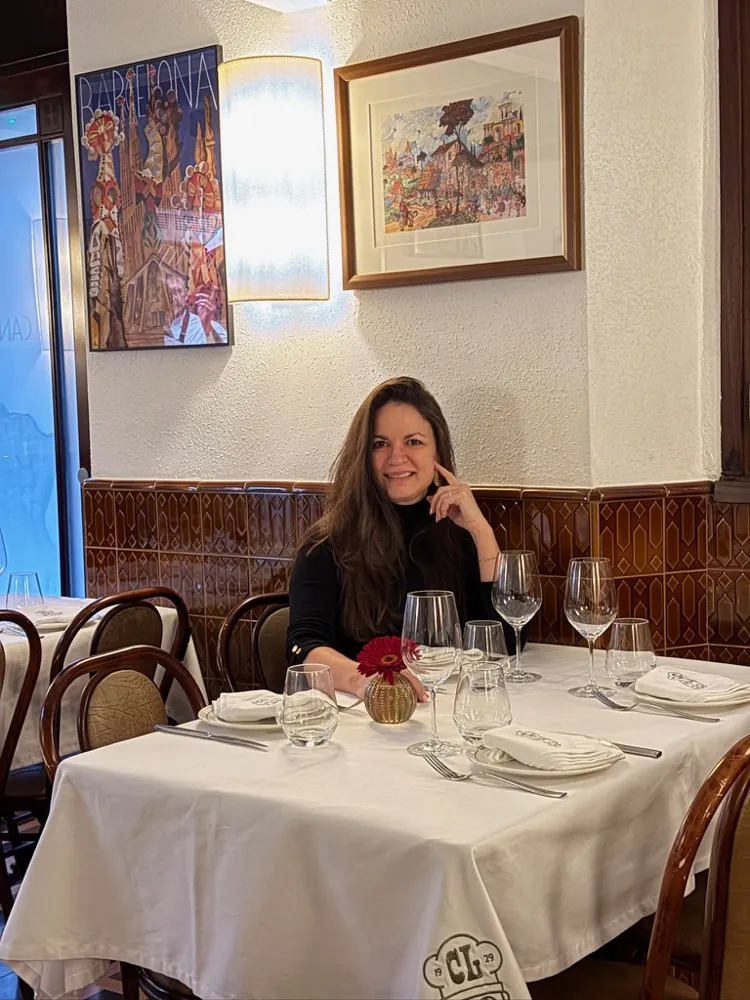 Mujer sentada a una mesa con mantel blanco en el comedor de Can Lluís, con cuadros en la pared y zócalo de azulejos