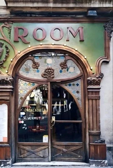 Puerta modernista del Grill Room en Escudellers, con el rótulo ROOM, arco de madera, vidrieras de colores y el letrero de vermut