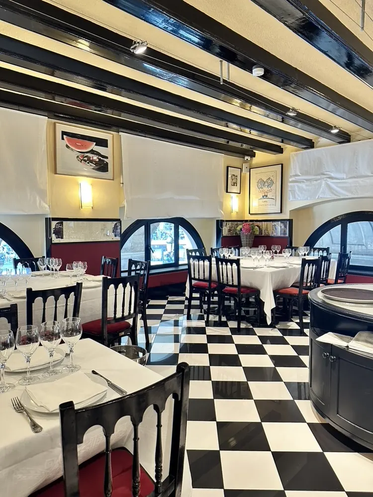Comedor de 7 Portes con suelo de baldosas blancas y negras, mesas con mantel blanco, vigas oscuras y ventanales en arco